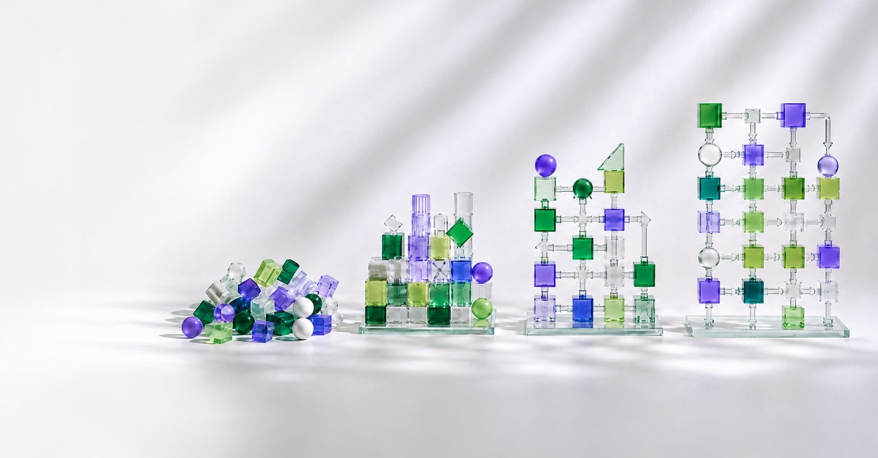 Four arrangements of translucent green and purple blocks, left to right: a loose pile, a stacked heap, a partly connected grid, and a tall grid where every block is linked by pipes and arrows.